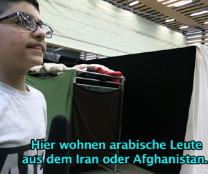 Foto eines Jungen, der vor einem Stockbett steht. Darunter die Schrift "Hier wohnen arabische Leute aus dem Iran oder Afghanistan".