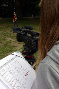 Foto einer Person, die hinter einer Videokamera steht und eine Checkliste in der Hand hält.