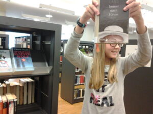 Ein Mädchen hält ein Buch mit einem abgeschnittenen Potrait-Foto so vor das Gesicht, dass ihr Kopf mit dem Buch zu verschmelzen scheint.