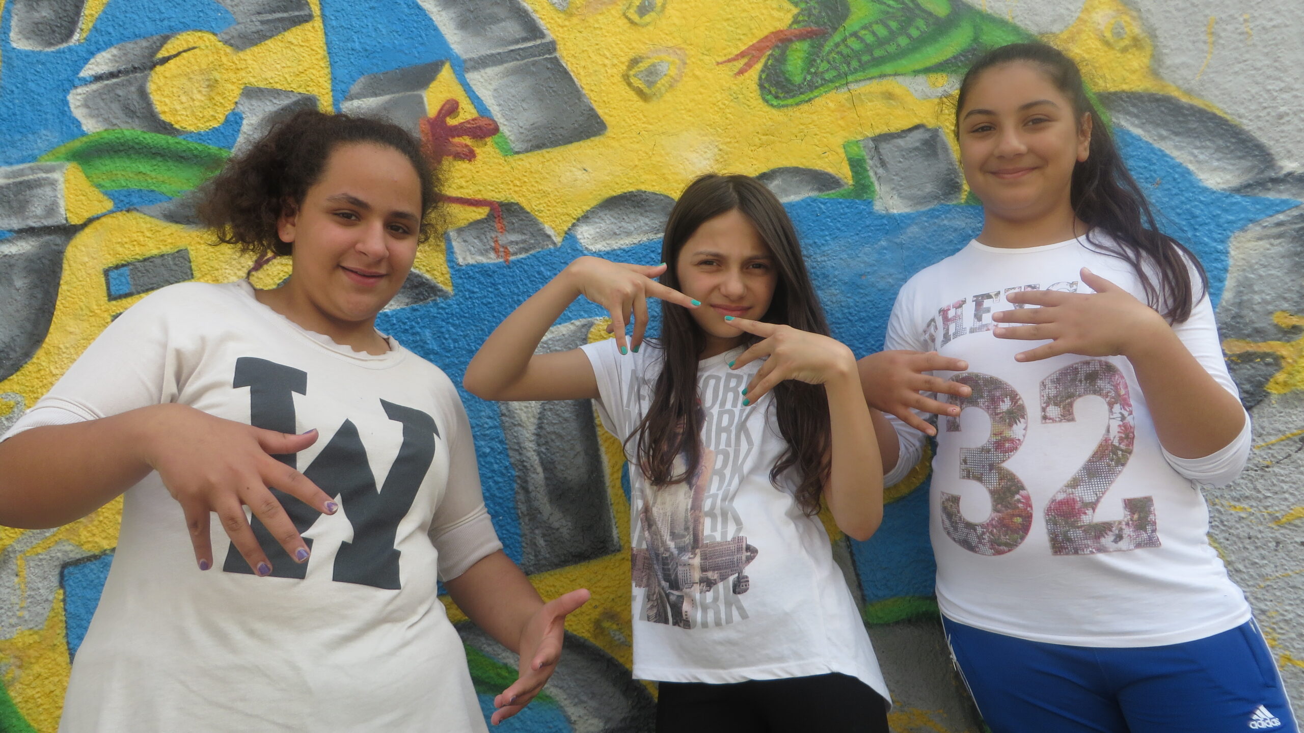 Drei Mädchen stehen in coolen Posen vor einer Graffiti-Wand.